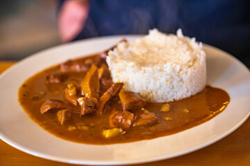 Sliced veal meat in spicy sauce with maize, rice on plate.