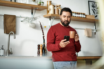 Elderly man enjoying a warm drink while browsing on his phone in a cozy kitchen