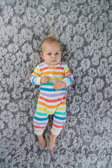 Fototapeta premium newborn baby girl playing with her feet, wearing a beautiful rainbow colored jumpsuit.