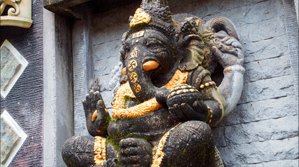 An old hindu stone statue of Ganesha covered with moss, standing on the str..