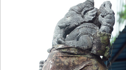 An old hindu stone statue of Ganesha covered with moss, standing on the str..