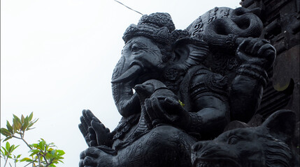An old hindu stone statue of Ganesha covered with moss, standing on the str..