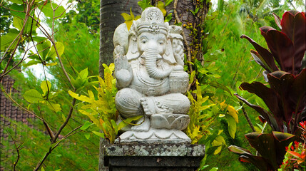An old hindu stone statue of Ganesha covered with moss, standing on the str..