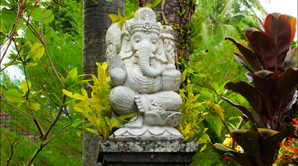 An old hindu stone statue of Ganesha covered with moss, standing on the str..