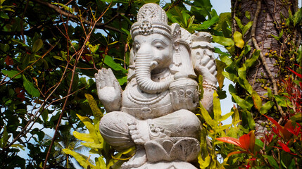 An old hindu stone statue of Ganesha covered with moss, standing on the str..