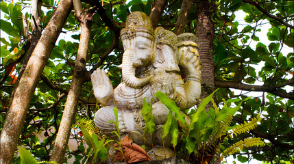 An old hindu stone statue of Ganesha covered with moss, standing on the str..