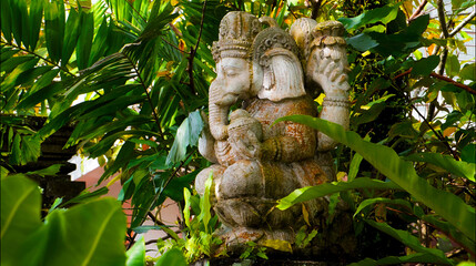 An old hindu stone statue of Ganesha covered with moss, standing on the str..