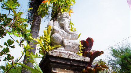 An old hindu stone statue of Ganesha covered with moss, standing on the str..