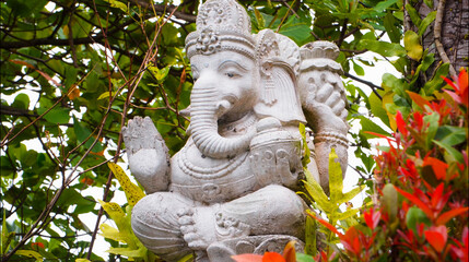 An old hindu stone statue of Ganesha covered with moss, standing on the str..
