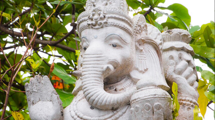 An old hindu stone statue of Ganesha covered with moss, standing on the str..