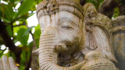 An old hindu stone statue of Ganesha covered with moss, standing on the str..