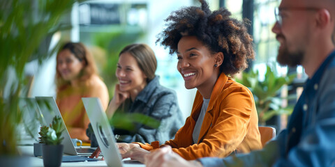 A smiling Black woman with curly hair participates in a collaborative meeting with colleagues in a bright, modern office.