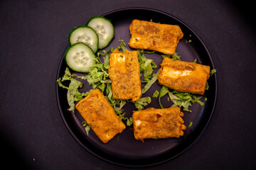Delicious Crispy Fried Paneer Pakora with Cucumber and Lettuce on Black Plate
