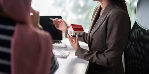 Real Estate Presentation and Home Buying. A real estate agent explains key features of a property using a model house during a meeting.