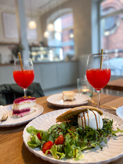 Cafe table with two orange cocktail drinks, two pieces of cake and a salad on a plate