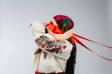 Woman in traditional attire conceals her face with a colorful scarf and red ribbon while expressing a cultural theme