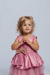 Cute girl in a pink dress with curls, posing confidently against a neutral background during a studio session