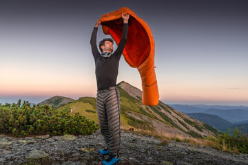 A traveler in the mountains spreads out an orange sleeping bag in the wind during an Alpenglow...