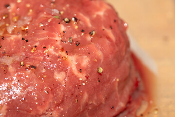Close up of a raw beef steak with sea salt and peppercorn seasoning on top