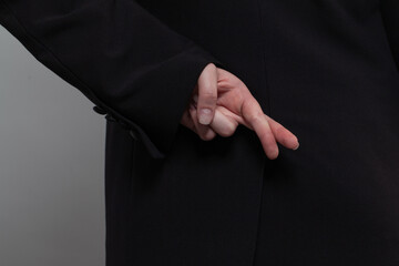 Businessman in black suit crosses his fingers behind his back on the plain grey background. Concept of corporate espionage, fraudulence and fake agreements