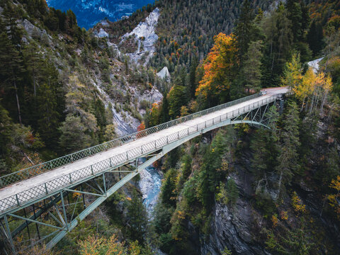 pedestrian bridge over deep canyon river, tall and steep rocks, autumnal colored trees, turquoise mountain water, adventure, overcoming challenges, gap, building bridges, concept, dramatic scenic aeri - Powered by Adobe