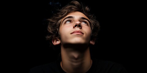 Fototapeta premium contemplative young man with brown hair gazes upward against stark background indoor stock.