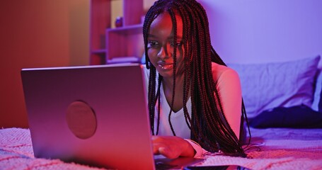 A teenager engaged in working on a laptop inside a cozy room that features LED lighting