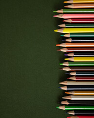Wooden colored pencils scattered on a green school desk