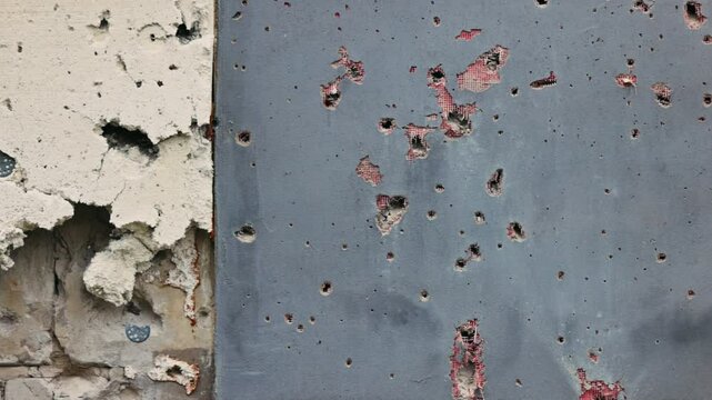 Holes from artillery shell fragments in the wall of an apartment building. Damage to a residential building as a result of artillery shelling. War in residential areas. Armed conflict in Ukraine