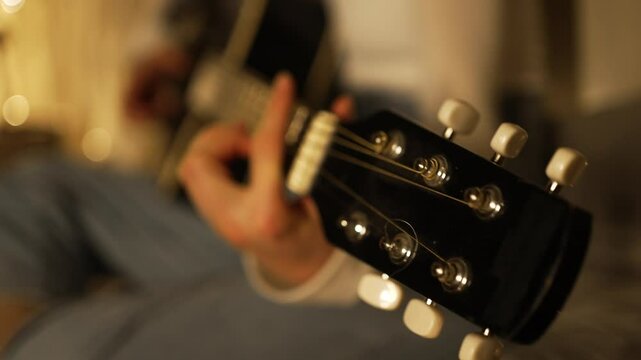 Musician performing acoustic guitar, focusing on headstock and tuning pegs, warm bokeh lights softly illuminating wooden instrument details and intimate musical moment