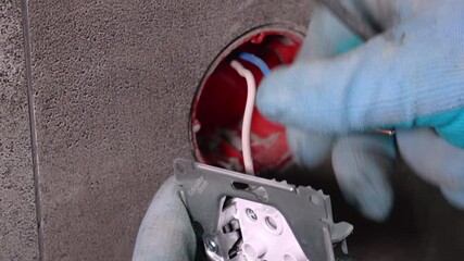 Electrician wearing protective gloves carefully installs new electrical outlet in concrete wall, connecting wires and securing outlet plate