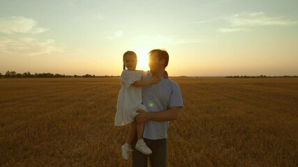 Father holding kid in arms in field at sunset. Happy cheery parent child kid strolling moving going across huge yellow meadow. Girl sits in man arms pointing with finger. Love fatherhood parenthood