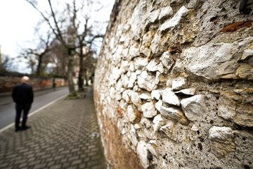 An old stone and brick wall in Kraków’s historic Kazimierz district, bearing the marks of time and history. The weathered stones and aged bricks, with cracks and moss growing between them, tell silent