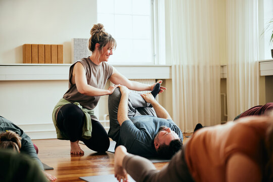 Teacher helping a student during yoga. She holds his leg and helps him bring his knee further down towards his chest.