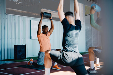Trainer leading a group of diverse fit young men through strength training exercises using a roller during a class at the gym