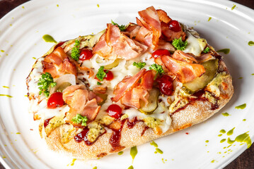 Delicious pizza topped with crispy bacon, cherry tomatoes, pickles, and fresh herbs, drizzled with a green sauce on a white plate, beautifully presented.
