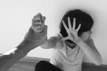 black and white photography frightened young girl in a pink shirt sits against a wall, raising her...
