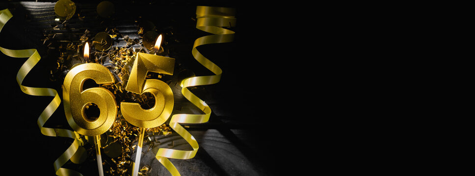 Golden candles number sixty-five burning brightly, celebrating 65th birthday anniversary. Festive ribbons and confetti on black background, creating elegant celebratory banner.