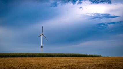 Obraz premium Wind turbine in a field under a blue sky.