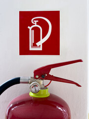 A red fire extinguisher placed under a fire extinguisher bracket on a white wall. The extinguisher...