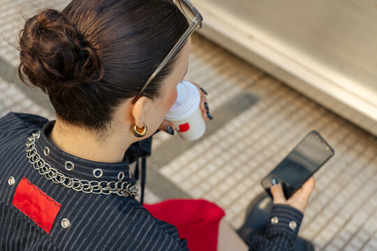 Fashionable designer drinking coffee and browsing smartphone