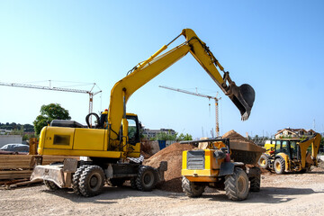Fototapeta premium Tivat, Montenegro - 06.22.2024: the excavator picks up and unloads soil into the loader