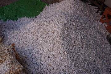 The freshly roasted puffed rice is spread over the ground on a plastic in a market setting likely...