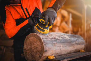 Man hand grinding with cordless wood grinder. Woodwork with aku grinder. Close up of grinder. Man dressed in reflective workwear. Close up of sanding a wood with orbital sander at workshop.