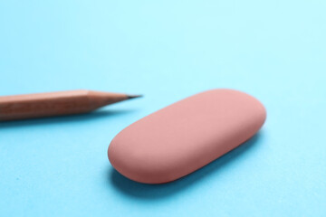 Eraser and pencil on light blue background, closeup