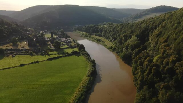 Drone footage flying up the River Wye on a bright summers day featuring Tintern Abbey