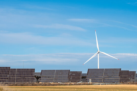 Wind turbine and solar panels working together in a hybrid renewable energy system under a clear sky.