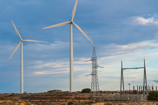 Multiple wind turbines and power lines against a dynamic sky, showcasing the intersection of clean energy and electrical grids.