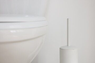 Toilet and brush near white wall, closeup