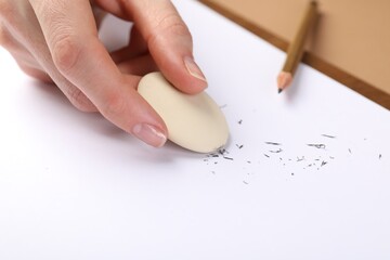 Woman rubbing eraser against paper at brown table, closeup